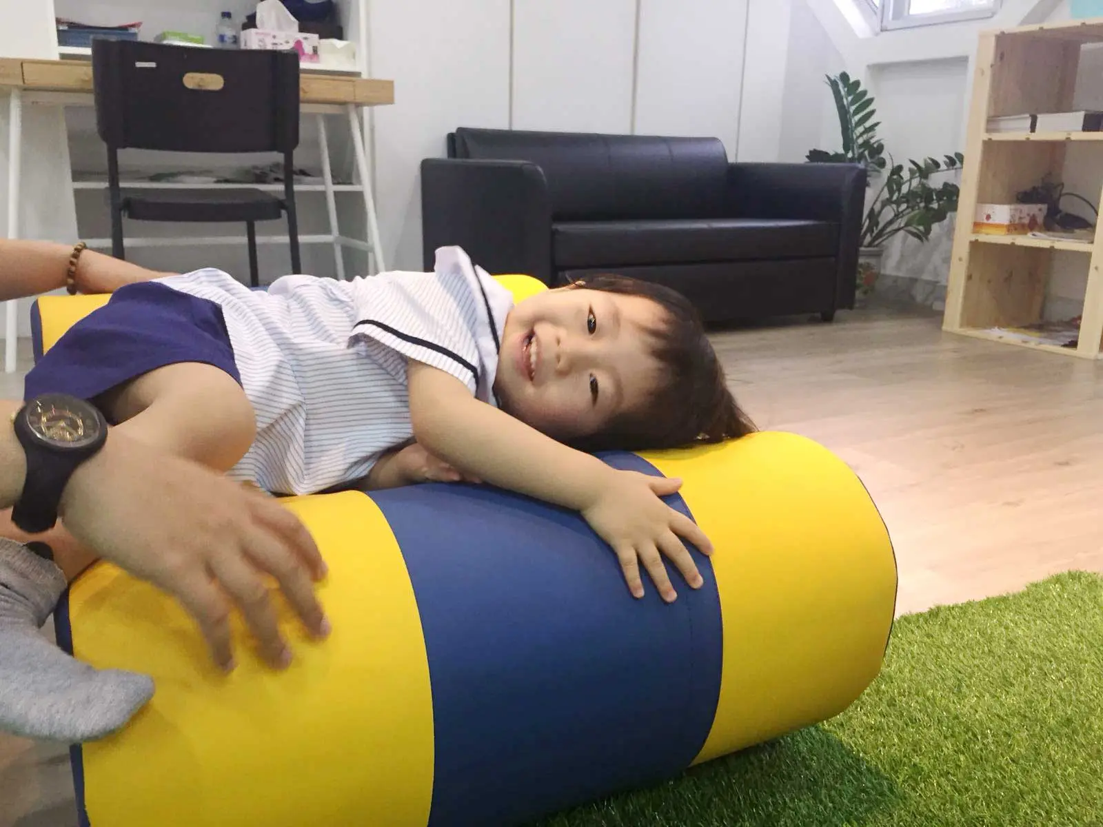 やわらかい青と黄色の遊具の円柱に横たわるプリスクールの子ども。