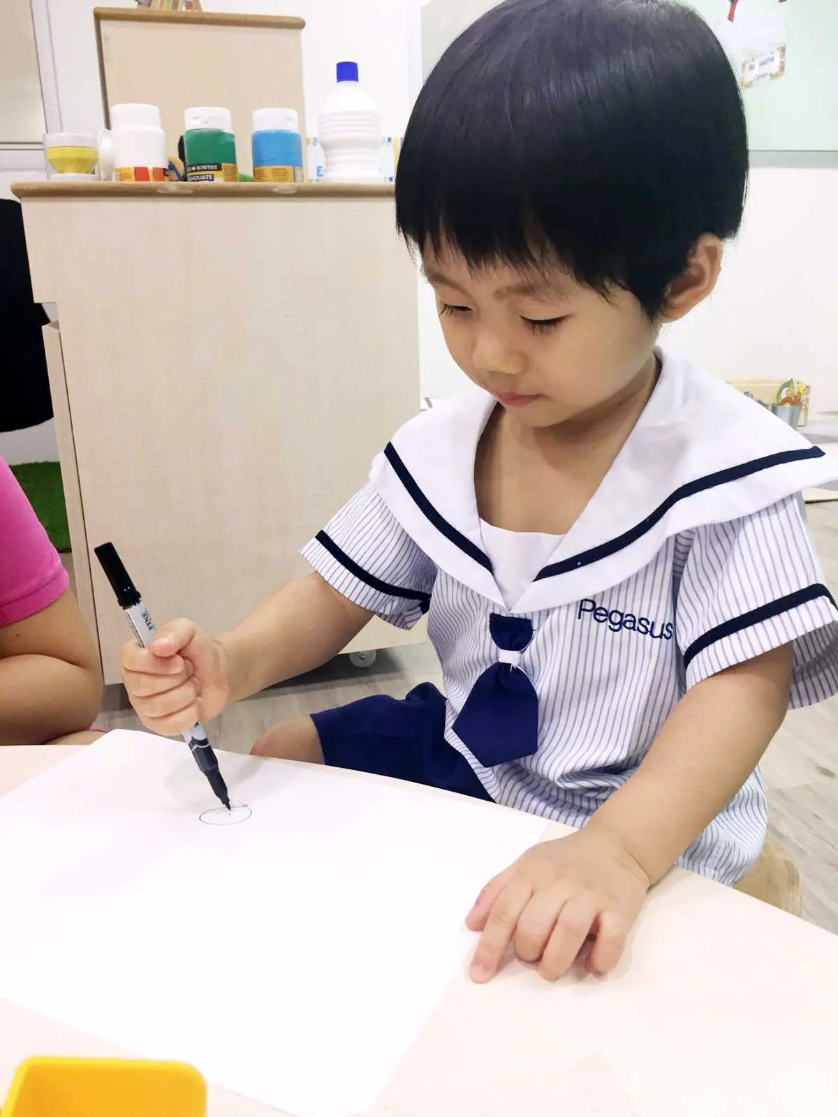 教室のテーブルでマーカーを使って丸を描く幼い子ども。