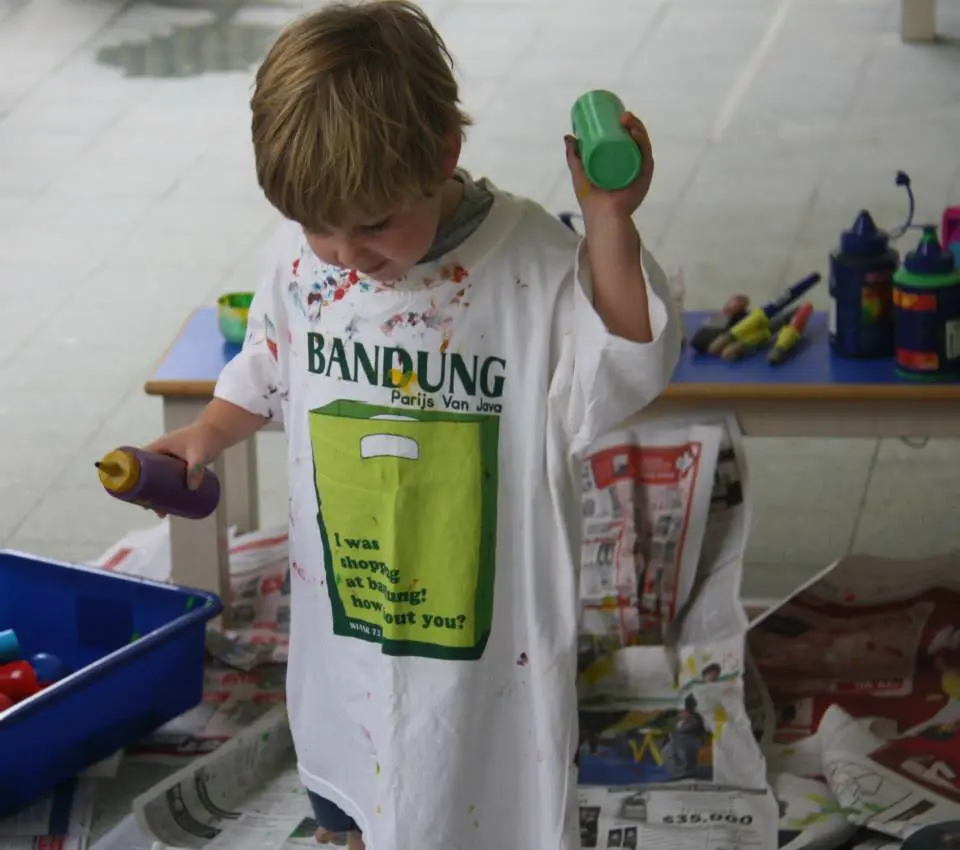 Child holding two paint bottles during a large-scale painting activity.