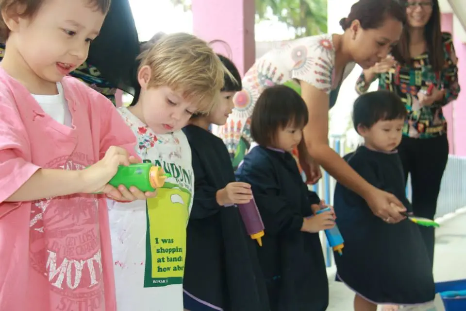 Children holding colourful paint bottles during a group art activity.