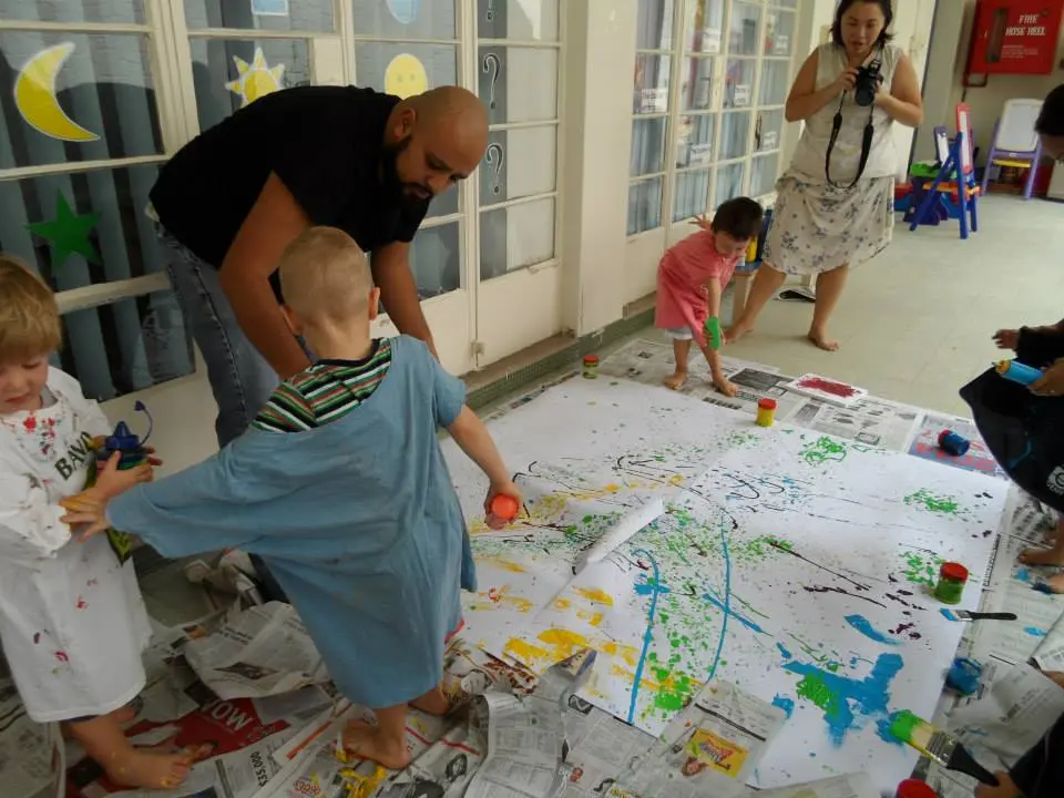 Preschool group creating a large abstract painting with adult support.
