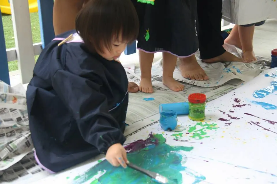Preschool child painting blue and green areas with a broad brush.