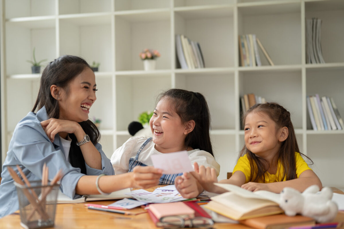 Two children laughing while learning English alphabet flashcards with a teacher at Pegasus